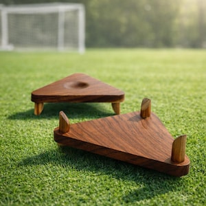 May include: Two triangular wooden display stands with a dark brown finish are placed on a green grassy surface. One stand has a small recessed area, the other has three upright supports. The stands are likely for displaying items.
