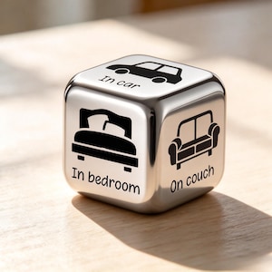 May include: A metallic cube with rounded edges featuring black icons and text on its faces. The visible sides display a car icon with the text In car, a bed icon with the text In bedroom, and a couch icon with the text On couch printed in black.
