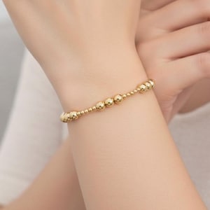 Op de afbeelding: Een gouden kralenarmband met een delicaat ontwerp. De armband heeft een reeks kleine, ronde kralen die aan elkaar zijn geregen, waardoor een eenvoudig maar elegant accessoire ontstaat. De armband wordt om een pols gedragen.