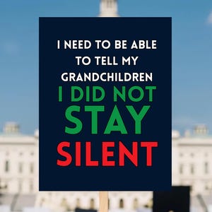 May include: A protest sign held up in front of a crowd and a government building. The sign is dark blue with white, green, and red text that reads: "I NEED TO BE ABLE TO TELL MY GRANDCHILDREN I DID NOT STAY SILENT."
