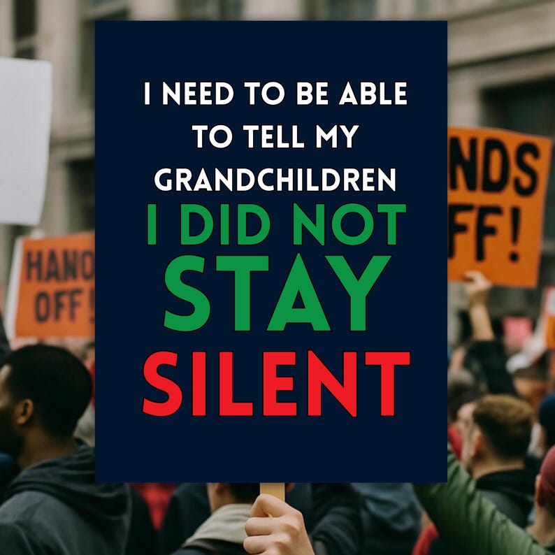 May include: A navy blue sign held up in a crowd with the text "I NEED TO BE ABLE TO TELL MY GRANDCHILDREN I DID NOT STAY SILENT" in white, green, and red. Other signs are visible in the background.