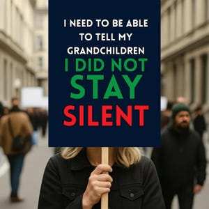May include: A person holding a sign with the text "I NEED TO BE ABLE TO TELL MY GRANDCHILDREN I DID NOT STAY SILENT." The sign has a dark blue background with white, green, and red text. The background shows a blurred street scene.