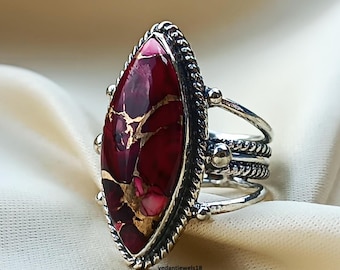 Könnte beinhalten: Silberner Ring mit einem auffälligen, ovalen Edelstein in tiefen Rot- und Goldtönen. Der Ring hat ein detailliertes, strukturiertes Band mit mehreren Schichten und kleinen silbernen Akzenten. Der Edelstein ist der Mittelpunkt, gefasst in einem dekorativen Silberrahmen.
