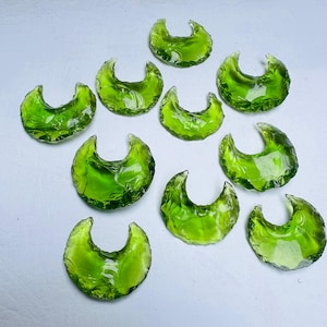 Pode incluir: Uma coleção de dez peças de vidro translúcido verde-limão em forma de meias-luas. Cada peça apresenta uma superfície curva e lisa com bordas irregulares e facetadas que captam a luz, criando uma aparência vívida e brilhante.