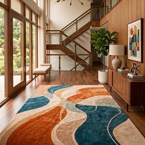 May include: A rectangular area rug featuring a large-scale abstract pattern with flowing, organic shapes in shades of deep teal, burnt orange, and beige. The rug has a textured pile and is positioned on a dark wood floor in a bright room.