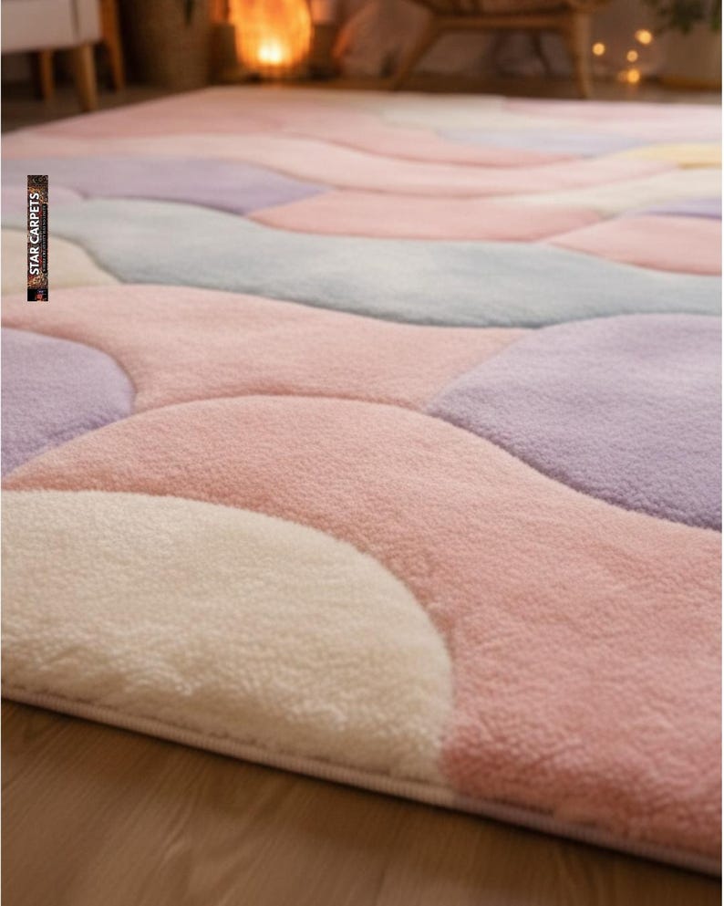 May include: A plush, pastel-colored area rug with a unique, flowing design. The rug features soft, rounded shapes in shades of pink, lavender, gray, and cream. The texture appears fluffy and inviting, suggesting a comfortable and stylish floor covering.