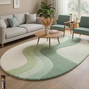 May include: An oval rug with a wavy design in shades of green and white. The rug is in a living room with a grey sofa, two armchairs, and a wooden coffee table. The rug has the text "STAR CARPETS" on the bottom left.