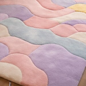 May include: A pastel-colored area rug with an abstract design. The rug features flowing, organic shapes in shades of pink, lavender, blue, and cream. The soft, plush texture and muted color palette create a calming and inviting aesthetic. The rug is a decorative floor covering.
