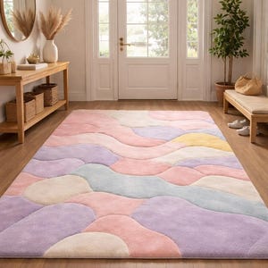 May include: A large, rectangular area rug with a pastel color palette of pink, purple, yellow, and blue. The rug features an abstract, flowing design, adding a soft and inviting touch to the hardwood floor in the entryway.