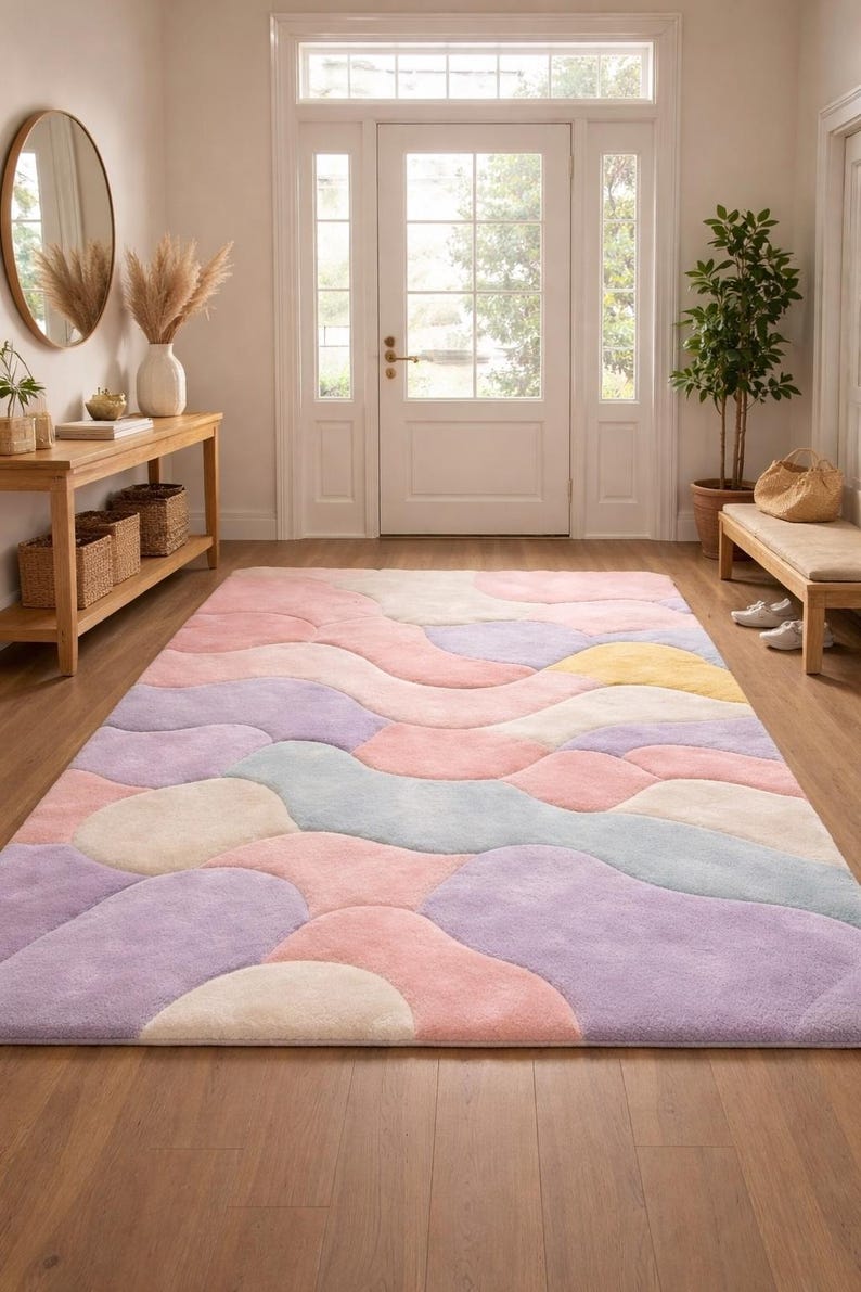 May include: A large, rectangular area rug with a pastel color palette of pink, purple, yellow, and blue. The rug features an abstract, flowing design, adding a soft and inviting touch to the hardwood floor in the entryway.
