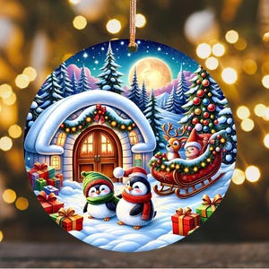 May include: A round Christmas ornament featuring a winter scene with a house, penguins, and a sleigh with reindeer. The ornament has a gold string for hanging and is decorated with a festive holiday theme.