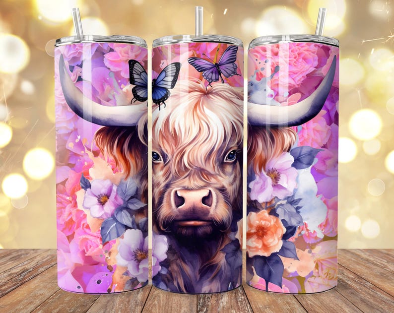 May include: Three stainless steel tumblers with a floral and Highland cow design. The design features a cow's face with large horns, butterflies, and pink and purple flowers. Each tumbler has a silver straw.