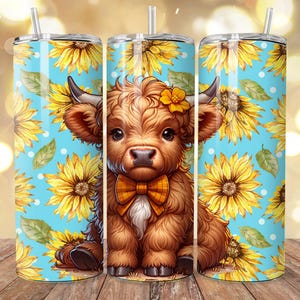 May include: Three stainless steel tumblers with straws. Each tumbler features a cartoon illustration of a Highland cow with a bow tie, set against a blue background with sunflowers and white polka dots. The tumblers are on a wooden surface.