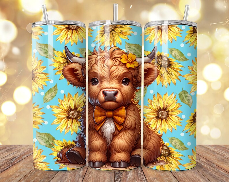 May include: Three stainless steel tumblers with straws. Each tumbler features a cartoon illustration of a Highland cow with a bow tie, set against a blue background with sunflowers and white polka dots. The tumblers are on a wooden surface.