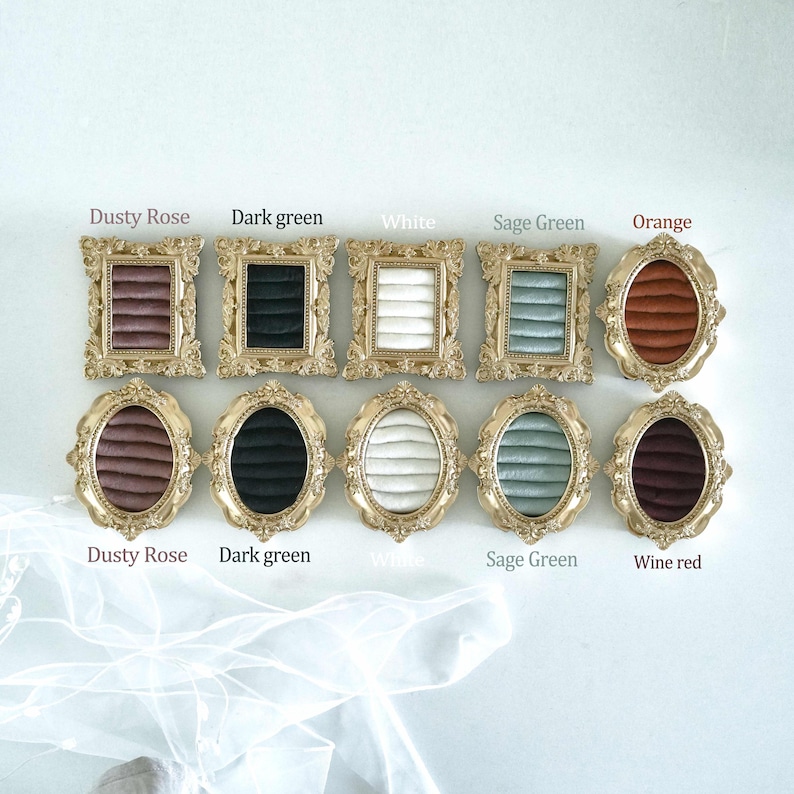 May include: Ten ornate gold-toned frames with velvet ring inserts in various colors including dusty rose, dark green, white, sage green, orange, and wine red. The top row features rectangular frames, while the bottom row contains oval frames.