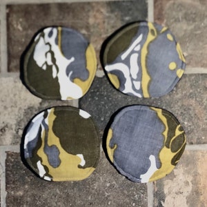 May include: Four round fabric patches with a camouflage pattern in shades of gray, yellow, and green. The patches are made of a soft, textured fabric.