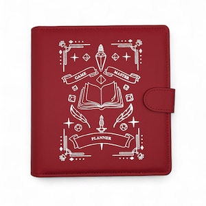May include: A burgundy planner with a white graphic design featuring an open book, dice, feathers, and a dagger. The words "Game Master" and "Planner" are displayed on banners. The planner has a snap closure.
