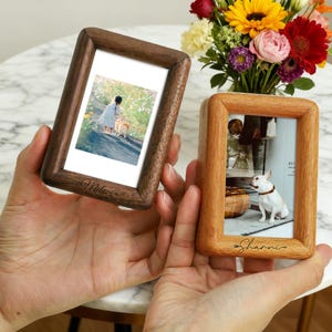 May include: Two wooden photo frames, one dark brown and one light brown, each holding a photograph. The dark brown frame has the name "Melia" engraved. The light brown frame has the name "Sharnni" engraved. A bouquet of flowers is in the background.