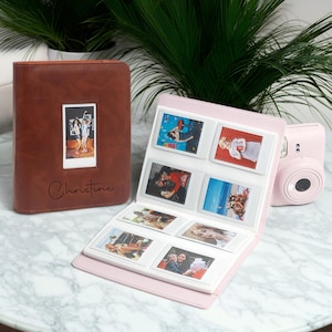 May include: A brown leather photo album with a photo and the name "Christine" in script. A pink photo album with several photos is open next to it. A pink instant camera is also in the image.