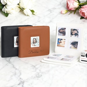 May include: Photo albums in black and brown leather with a square photo window. The brown album has the name "Bubba" and a heart symbol. A white album with photos and a Polaroid camera are also in the image.