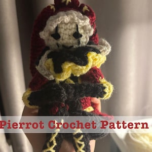 Könnte beinhalten: Handgefertigte Pierrot-Puppe aus Häkelarbeit mit weißem Gesicht, schwarzen Augen und einem rot-schwarzen Outfit. Die Puppe hat einen gelben Kragen und einen passenden Hut. Der Text "Pierrot Crochet Pattern" wird unten angezeigt.
