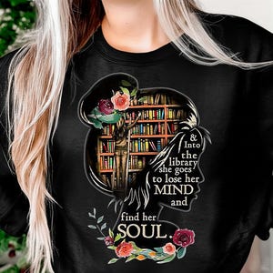 May include: Black sweatshirt featuring a silhouette of a woman with a library inside her head. The design includes the text "& Into the library she goes to lose her MIND and find her SOUL" with floral accents.