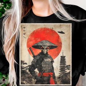May include: Black sweatshirt featuring a graphic of an alien samurai with a katana, wearing a traditional Japanese hat, set against a red sun and pagoda background. The image includes the text "宇宙客人".