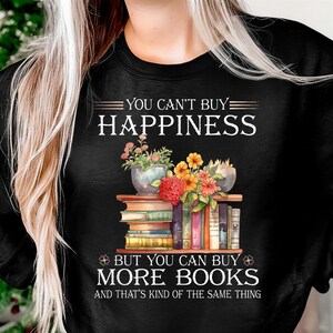 May include: Black sweatshirt with the text "YOU CAN'T BUY HAPPINESS BUT YOU CAN BUY MORE BOOKS AND THAT'S KIND OF THE SAME THING." The graphic features a stack of books with flowers and plants on top.