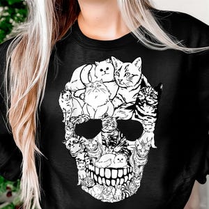May include: Black sweatshirt featuring a skull design composed of various cat illustrations in black and white. The cats are arranged to form the shape of a skull, with details like eyes, nose, and teeth. The design is centered on the front of the sweatshirt.