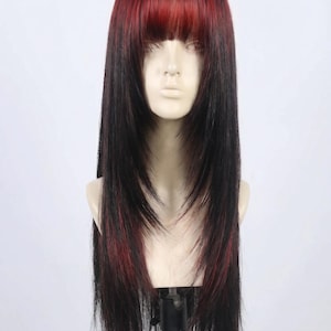 May include: A long, layered wig with a black base and red highlights. The wig features a blunt, red fringe and is displayed on a mannequin head. The hair is styled with long, flowing layers.