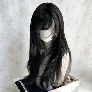 May include: A black wig with long, layered hair and bangs, displayed on a mannequin head. The wig has a natural-looking hairline and is styled with a slight wave. The wig is likely made of synthetic fibers and is designed for cosplay or fashion.