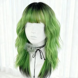 Puede incluir: Peluca verde y negra con textura ondulada y flequillo. La peluca está peinada en una cabeza de maniquí, con un collar gargantilla negro con una flor gris y una cinta negra. El degradado de color de la peluca pasa de negro en las raíces a verde vibrante.