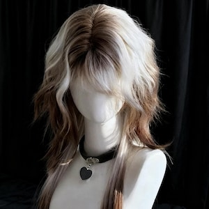 Könnte beinhalten: Eine mehrfarbige Perücke mit braunen, blonden und weißen Strähnen. Die Perücke hat einen Pony und eine wellige Textur. Ein schwarzes Halsband mit Herzanhänger wird auf einem Schaufensterkopf getragen.