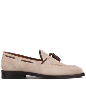 Op de afbeelding: Beige su&egrave;de loafer met een donkerbruine zool en afwerking. De schoen heeft een decoratieve kwast en gestikte details. Een klassieke instapper voor dagelijks gebruik.