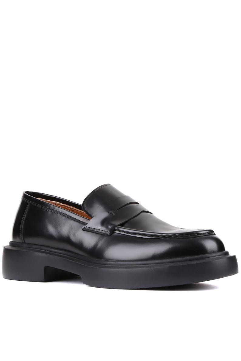 Puede incluir: Mocas&iacute;n de cuero negro con suela gruesa. El zapato presenta un dise&ntilde;o cl&aacute;sico de mocas&iacute;n con borlas, con punta redondeada y una correa en el empeine. La suela tiene aproximadamente 3,8 cm de grosor.