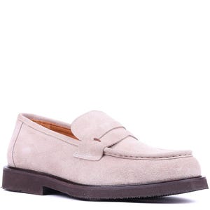May include: A light beige suede loafer with a dark brown sole. The shoe features a classic penny loafer design with a strap across the vamp. The shoe is a neutral color and suitable for various outfits.