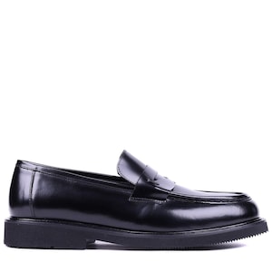 May include: A pair of black leather penny loafers. The shoes have a classic design with a rounded toe, a strap across the vamp, and a thick, textured sole. The loafers are made of shiny, polished leather.
