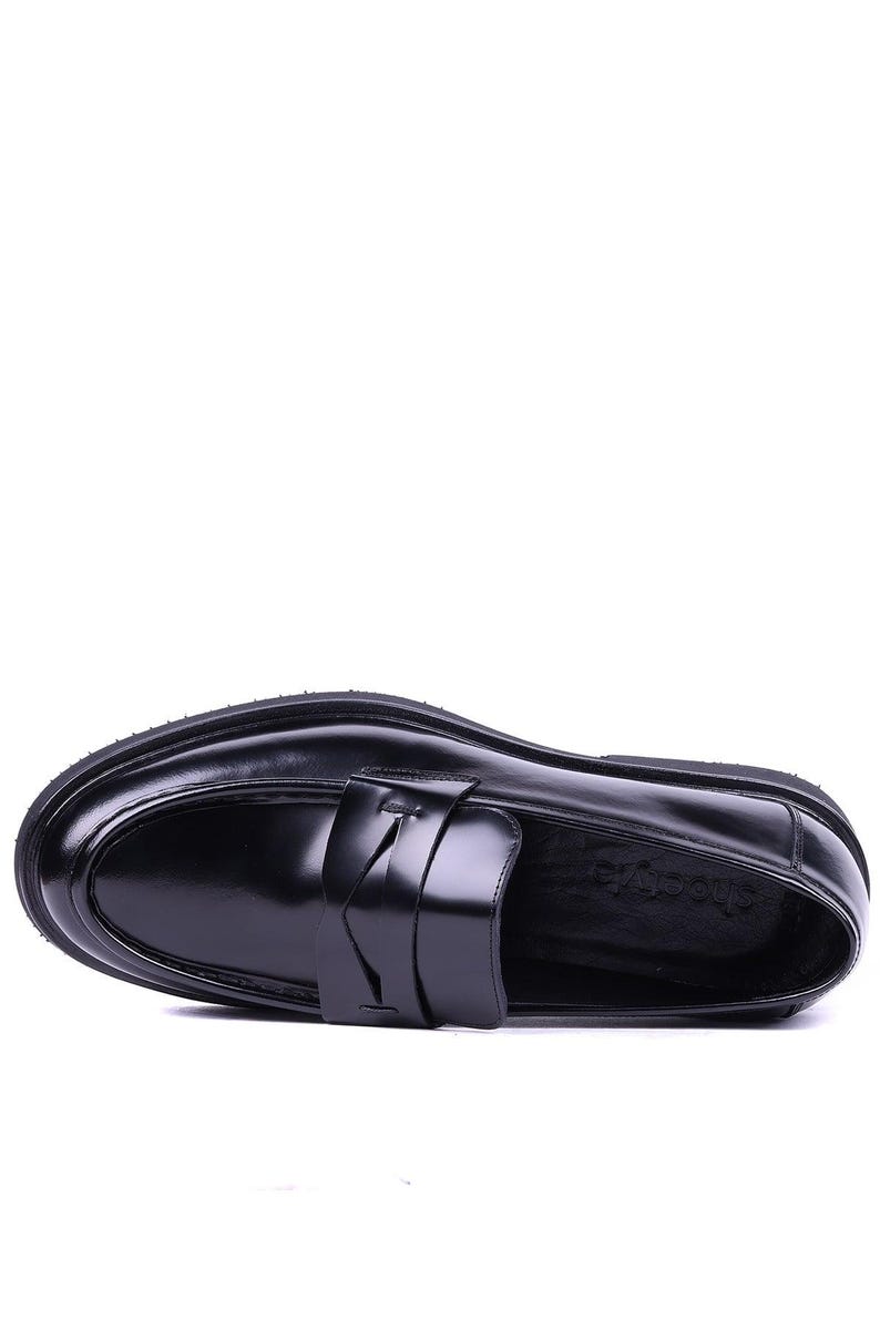 May include: A black leather loafer with a rounded toe and a thick sole. The shoe features a strap detail across the top. The shoe is approximately 11 inches long.