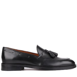 Op de afbeelding: Een zwarte leren loafer met een kwastje. De schoen heeft een ronde neus en een lage hak. Het leer is gepolijst en glanzend. De schoen is geschikt voor formele of zakelijke kleding. Ongeveer 28 cm lang.