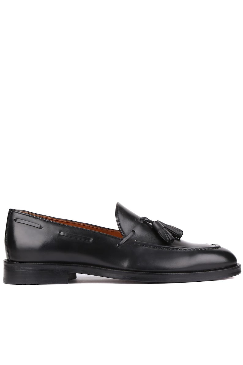Op de afbeelding: Een zwarte leren loafer met een kwastje. De schoen heeft een ronde neus en een lage hak. Het leer is gepolijst en glanzend. De schoen is geschikt voor formele of zakelijke kleding. Ongeveer 28 cm lang.