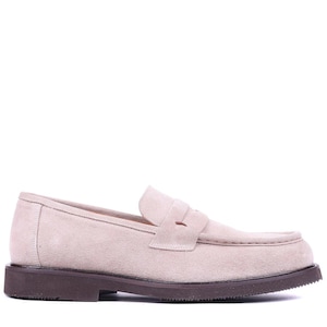 May include: A light beige suede loafer with a dark brown sole. The shoe features a classic penny loafer design with a rounded toe and a strap across the vamp. The sole is approximately 1 inch thick.