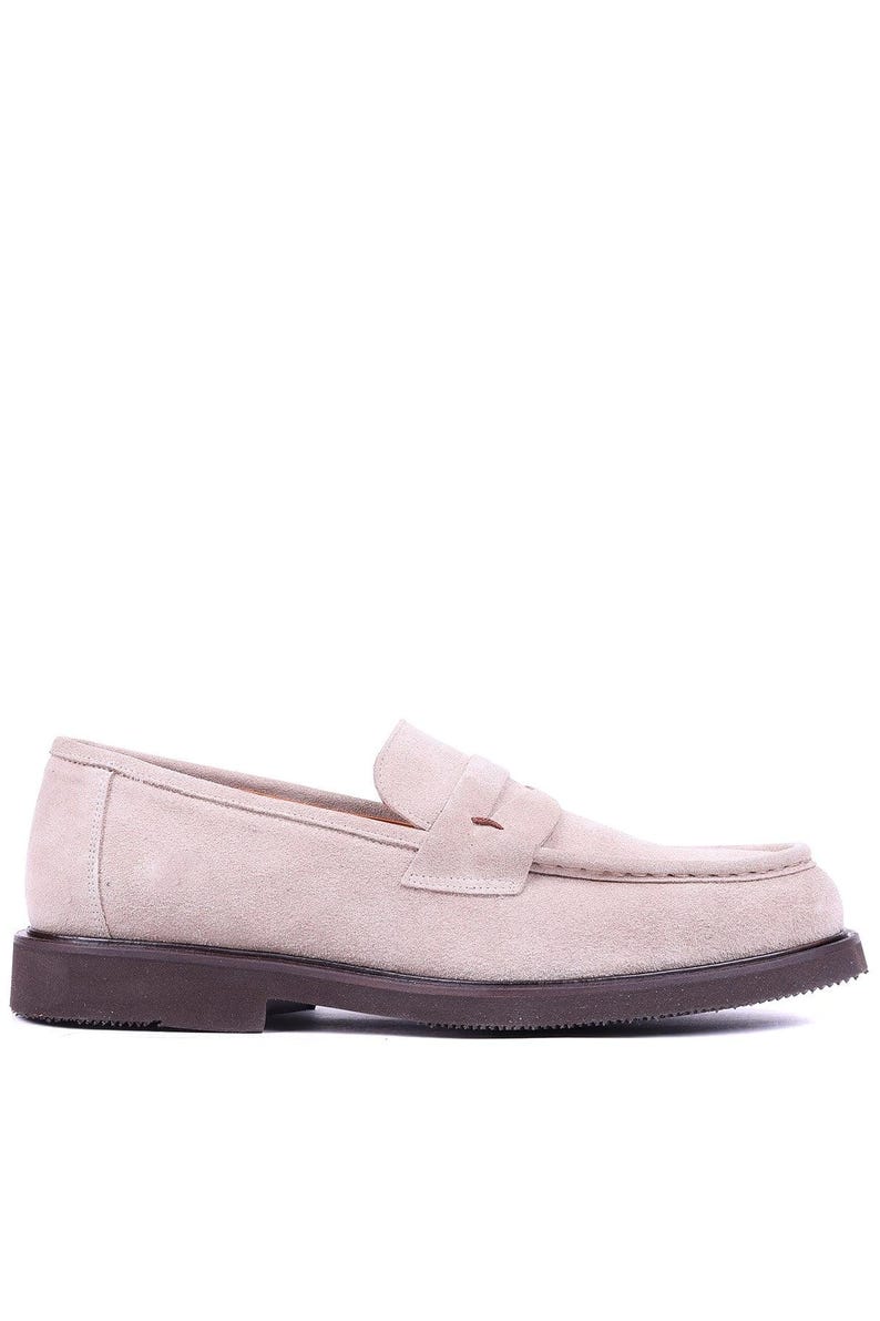 May include: A light beige suede loafer with a dark brown sole. The shoe features a classic penny loafer design with a rounded toe and a strap across the vamp. The sole is approximately 1 inch thick.