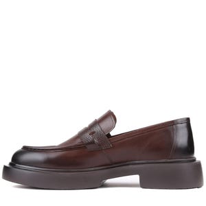 Puede incluir: Mocas&iacute;n de cuero marr&oacute;n con suela gruesa. El zapato presenta una correa texturizada en la parte superior y una puntera redondeada. La suela tiene aproximadamente 3,8 cm de grosor.