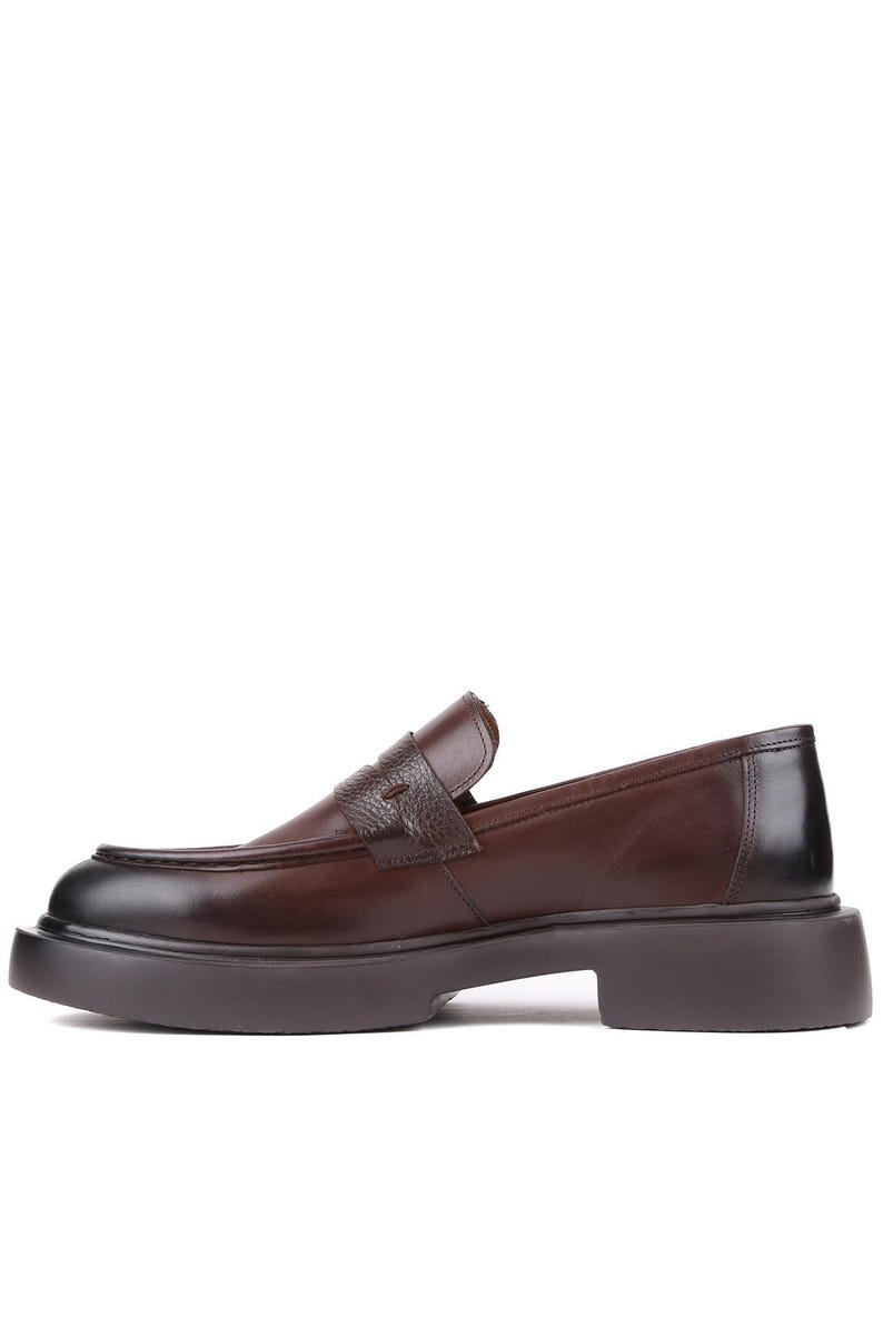 Puede incluir: Mocas&iacute;n de cuero marr&oacute;n con suela gruesa. El zapato presenta una correa texturizada en la parte superior y una puntera redondeada. La suela tiene aproximadamente 3,8 cm de grosor.