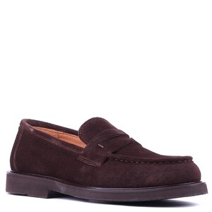 May include: A single brown suede loafer with a rounded toe and a low, dark brown sole. The shoe features a penny strap detail across the vamp and a stitched design. The shoe is designed for comfort and style.
