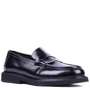 May include: Black leather penny loafers with a rounded toe and a thick, flat sole. The shoes have a classic design with a strap across the vamp. The loafers are a versatile footwear option.