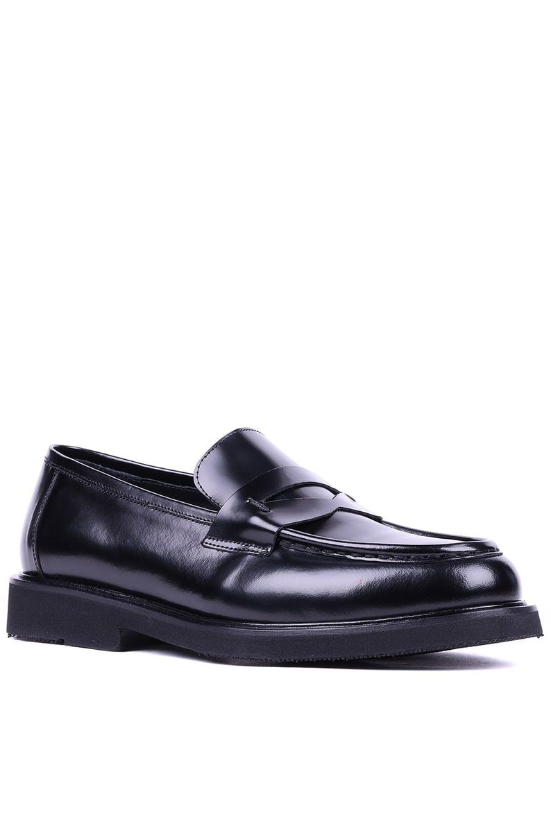 May include: Black leather penny loafers with a rounded toe and a thick, flat sole. The shoes have a classic design with a strap across the vamp. The loafers are a versatile footwear option.