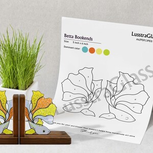 Può includere: Ferma libri a forma di pesce Betta in vetro colorato con accenti gialli, arancioni e blu, su una base di legno. I fermalibri misurano 12,7 cm per 15,2 cm. Sullo sfondo sono visibili un diagramma e una tavolozza di colori.