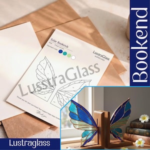 Può includere: Reggilibri a forma di farfalla con ali in vetro colorato blu, verde acqua e verde. I reggilibri in legno misurano 12,7 cm x 15,2 cm. L'immagine mostra anche un diagramma delle ali di farfalla e il testo "LustraGlass".