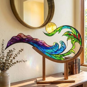 May include: A stained glass sculpture depicting a wave with a sun and foliage. The wave features shades of blue, purple, and green, set in a wooden frame. The sculpture is displayed on a wooden surface.